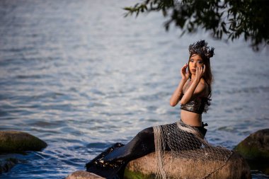 Deniz kıyısındaki Kayalıklarda Deniz Kızına Takılan Asyalı Denizkızı, Deniz Kabuğu desenli taç ve Kara Parlak Kuyruk ile Deniz Kraliçesi sıfatıyla süslenmiş. Yatay Resim