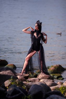 Siyah Elbiseli Genç Esmer Dansçı Rocky Shore 'da Dans Pasını Gösterirken Deniz Kabuğu Dekorasyonlu Taç ve İnci Kolye Giyiyordu. Dikey resim
