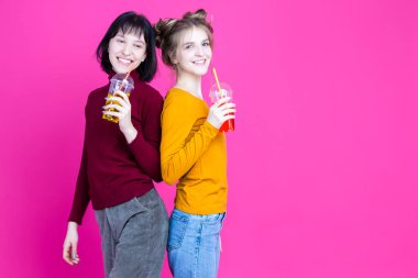 Pembe arka planda renkli meyve suyu ya da meyve suyu dolu bardaklarla poz verirken gülümseyen beyaz kız arkadaşlar birlikte eğleniyorlar. Yatay Resim