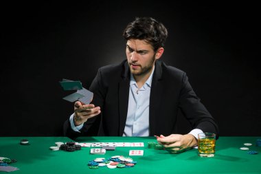 Yakışıklı, beyaz tenli poker oyuncusu poker masasında fiş ve kartlarla bahis oynuyordu. Yatay Resim Kompozisyonu