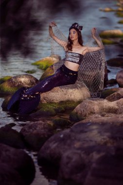 Asyalı Deniz Kızı Kayalıklarda Ağlı Poz Verirken Deniz kabuğu süslenmiş taç ve Siyah Parlak Kuyruklu Deniz Kraliçesi Sırtında Kurularak Vuruldu.