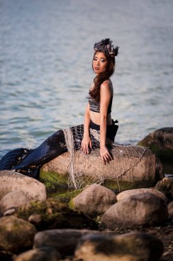 Deniz kıyısındaki Kayalıklarda Deniz Kızına Takılan Asyalı Denizkızı, Deniz Kabuğu desenli taç ve Kara Parlak Kuyruk ile Deniz Kraliçesi sıfatıyla süslenmiş. Dikey Resim Yönlendirmesi