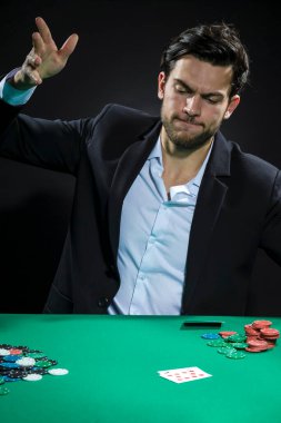 Genç, duygusal, beyaz tenli Brunet Poker oyuncusu poker masasında patates kızartması ve kartlarla oynarken. Dikey Resim Yönlendirmesi