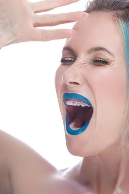 İpek derili, mavi saçlı, beyaz arka planda diş teli takan, gururla bağıran beyaz bir kadın. Dikey Resim Yönlendirmesi