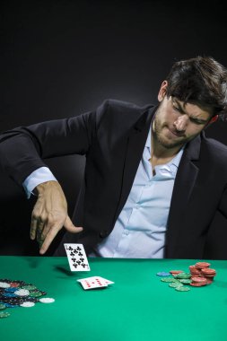Genç, duygusal, beyaz tenli Brunet Poker oyuncusu poker masasında patates kızartması ve kartlarla oynarken. Dikey Resim