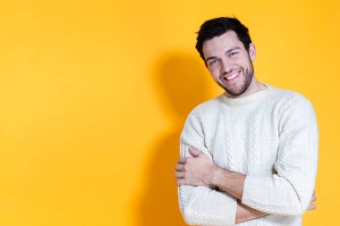 Gülümseyen komik, beyaz, örgü ören yakışıklı adam, mutlu bir şekilde gülümserken sarı arka planda poz veriyor. Yatay Resim