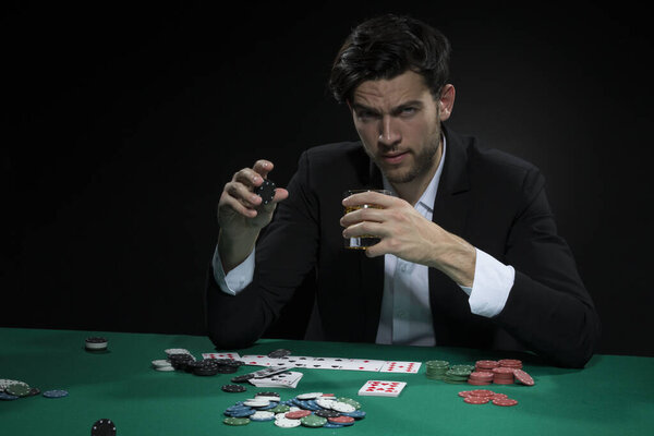 Концентрированный кавказский Брюнет Янг Покер Игрок за игровым столом с чипсами и картами во время питья алкоголя. Состав изображения