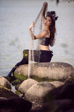 Rocky Deniz Kıyısı 'nda Ağlı Deniz Kızı, Deniz Kabuğu süslenmiş taç ve ince gövdesine siyah parlak bir kuyruk takıyor. Deniz Hanımefendisi kılığında. Dikey Resim Yönlendirmesi