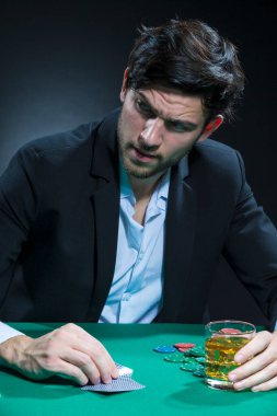 Cipslerle ve iskambil kağıtlarıyla poker masasında alkol içerken konsantre olmuş beyaz tenli Brunet Poker oyuncusu. Dikey Resim Kompozisyonu