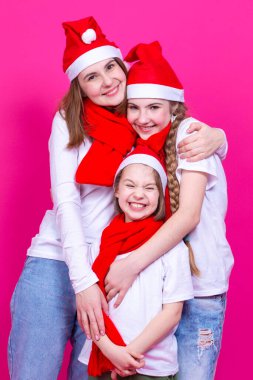 Tatil fikirleri ve kavramları. Birbirlerine sarılırken Noel Baba şapkası takan ve birlikte eğlenen üç mutlu beyaz kız. Dikey Çekim