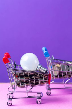 Tasarruf Enerjisi Konsepti olarak içi bozuk para ve ampul dolu iki tramvay arabası. Mor Arkaplan 'da. Dikey Çekim