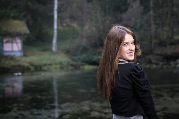 Junge Frau in Jacke blickt hinter ihre Schulter und lächelt auf den See — Stockfoto