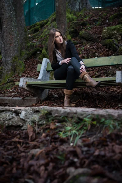 Mladá žena v bundě sedí na lavičce — Stock fotografie