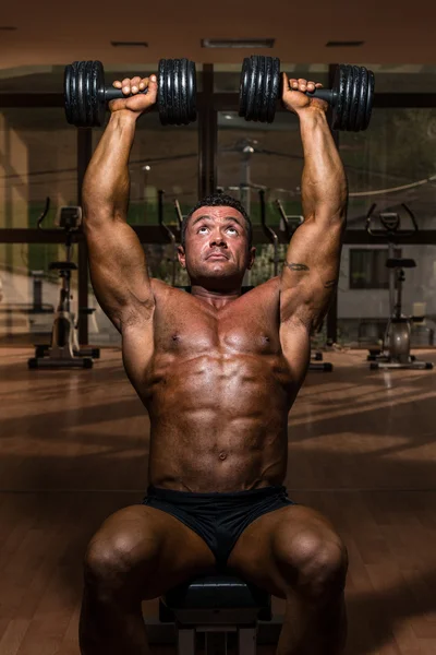 Male bodybuilder doing shoulder press whit dumbbell — Stock Photo, Image