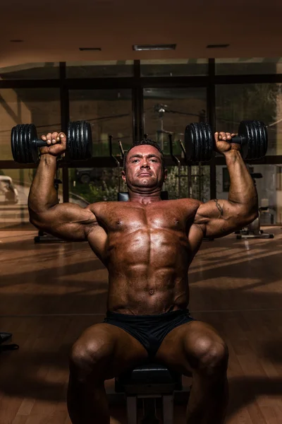 Male bodybuilder doing shoulder press whit dumbbell — Stock Photo, Image