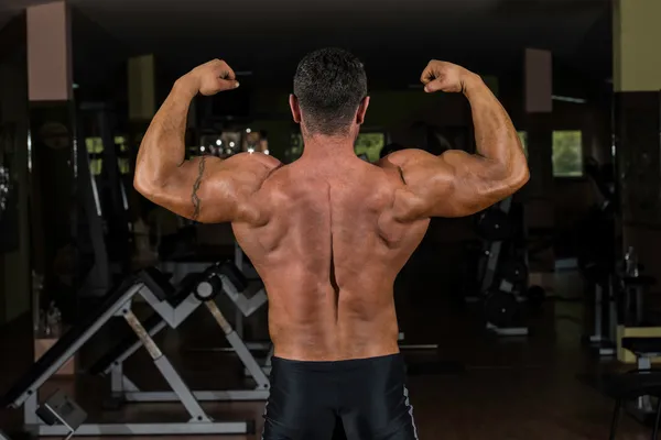 Muscular fisiculturista mostrando suas costas bíceps duplos — Fotografia de Stock