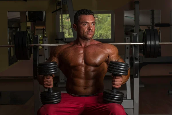 Shirtless body builder posing with dumbbell at the bench — Stock Photo, Image