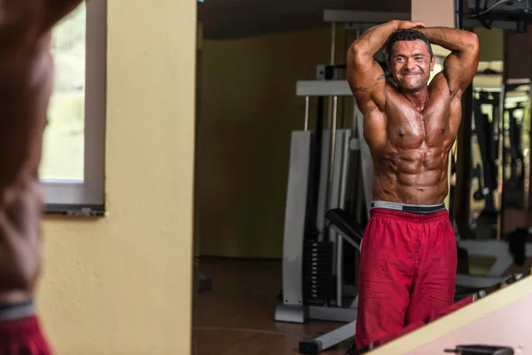Bodybuilder showing abs at mirror — Stock Photo, Image