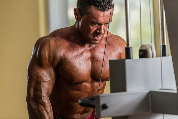 Bodybuilder doing heavy weight exercise for triceps with cable — Stock Photo, Image