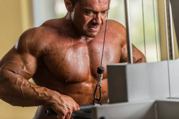 Bodybuilder doing heavy weight exercise for triceps with cable — Stock Photo, Image