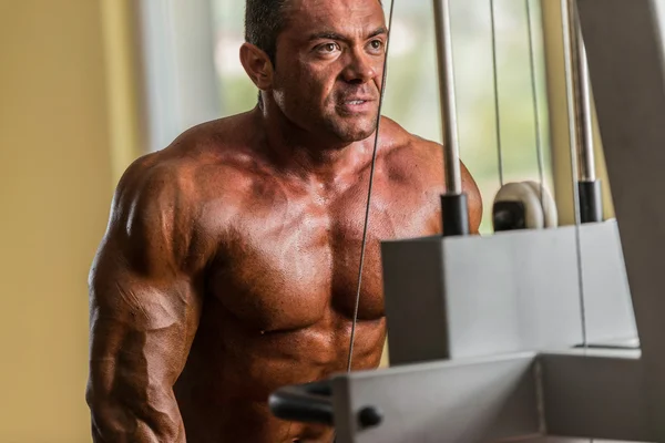 Bodybuilder doing heavy weight exercise for triceps with cable — Stock Photo, Image