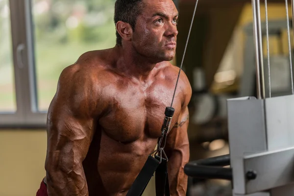 Bodybuilder doing heavy weight exercise for triceps with cable — Stock Photo, Image