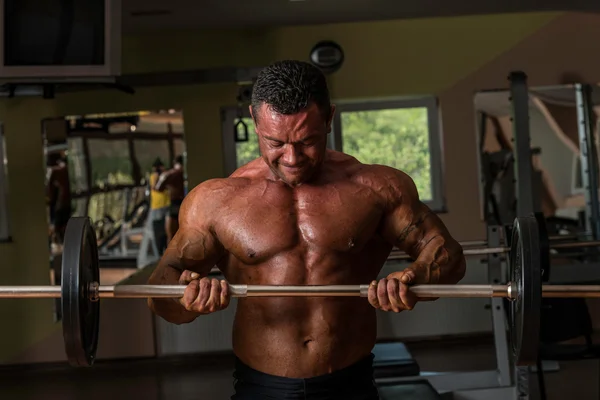 Bodybuilder doing heavy weight exercise for biceps with barbell — Stock Photo, Image