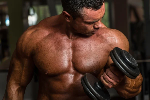 Shirtless construtor de corpo posando com halteres no banco — Fotografia de Stock