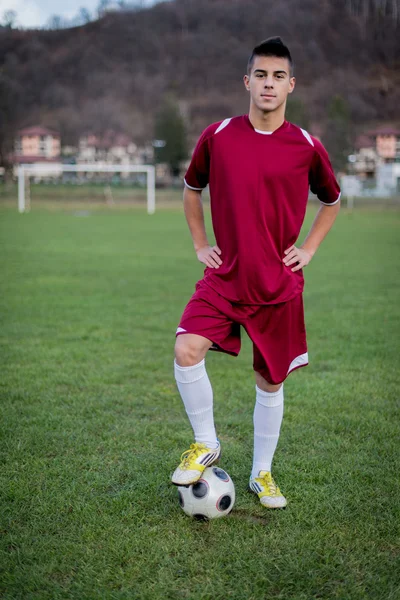 Молодий футболіст з м'ячем на полі в червоній сукні — стокове фото