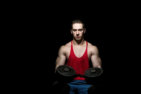 Young bodybuilder posing with dumbbell at the bench on black bac — Stock Photo, Image