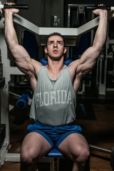 Young bodybuilder doing shoulder press on machine — Stock Photo, Image