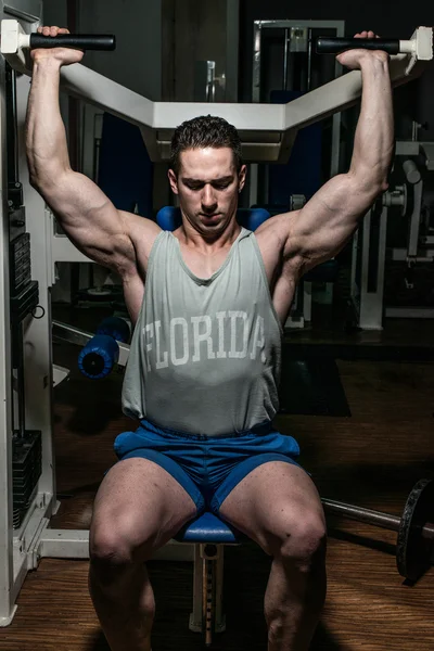 Young bodybuilder doing shoulder press on machine — Stock Photo, Image