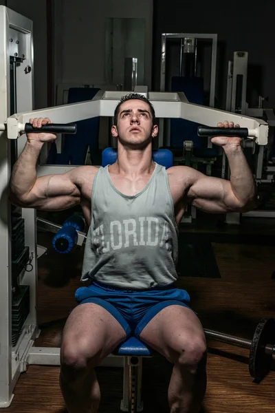 Young bodybuilder doing shoulder press on machine — Stock Photo, Image