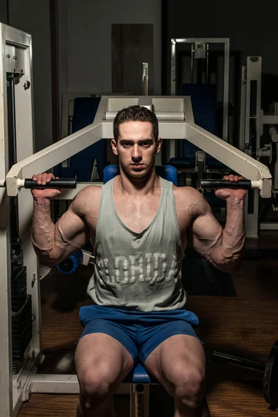 Young bodybuilder doing shoulder press on machine — Stock Photo, Image