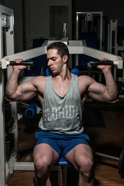 Young bodybuilder doing shoulder press on machine — Stock Photo, Image