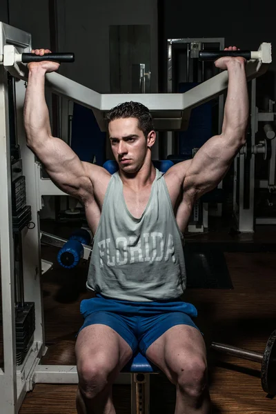 Young bodybuilder doing shoulder press on machine — Stock Photo, Image