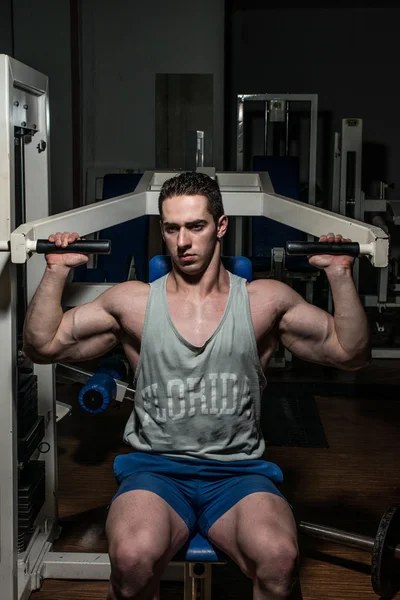 Young bodybuilder doing shoulder press on machine — Stock Photo, Image