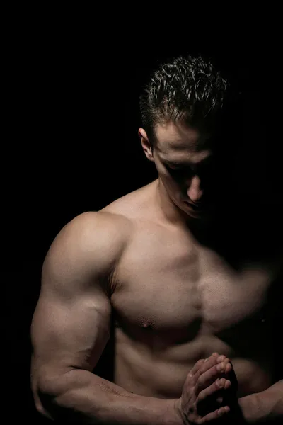 Strong man praying on black background — Stock Photo, Image