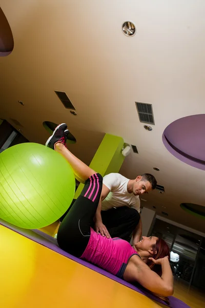 Jovem feliz exercitando na bola de fitness com trem pessoal — Fotografia de Stock