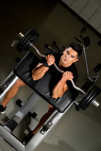 Young man in the gym exercising biceps with barbell — Stock Photo, Image