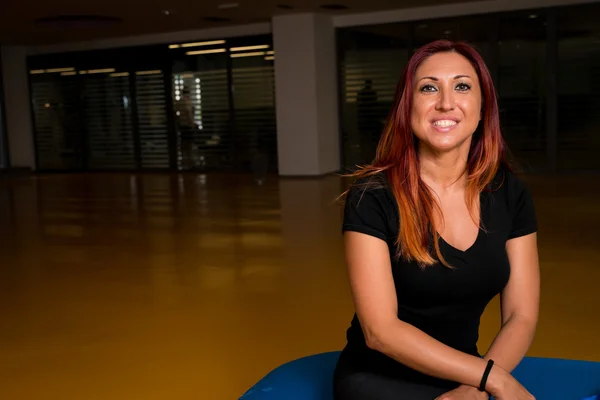 Portrait of a happy red haired woman posing while relaxing in a gym — Stock Photo, Image