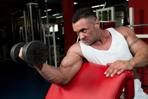 Homem no ginásio que exercita bíceps com halteres — Fotografia de Stock