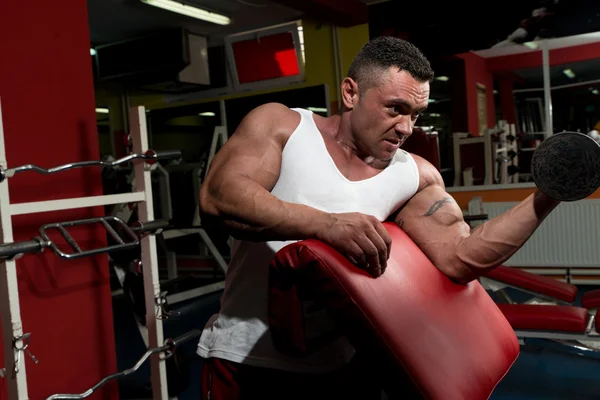 Homem no ginásio que exercita bíceps com halteres — Fotografia de Stock