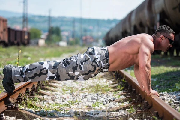 Schöner Mann macht Liegestütze an der Eisenbahn — Stockfoto