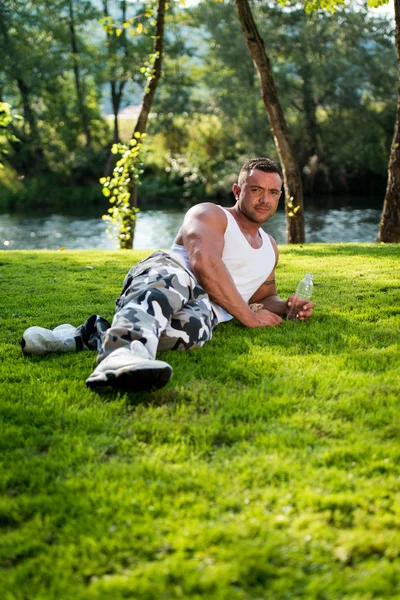 Mann liegt auf Gras und hält Wasserflasche — Stockfoto