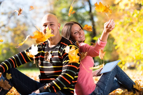 Mladý pár s sluchátka a házel na podzim listy — Stock fotografie