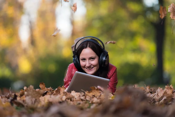 Mujer joven acostada afuera y escuchando auriculares —  Fotos de Stock