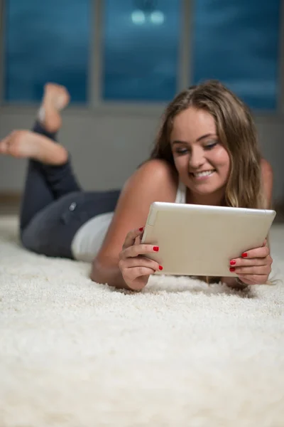 Glückliche Frau benutzt ipad, während sie auf Teppich liegt — Stockfoto