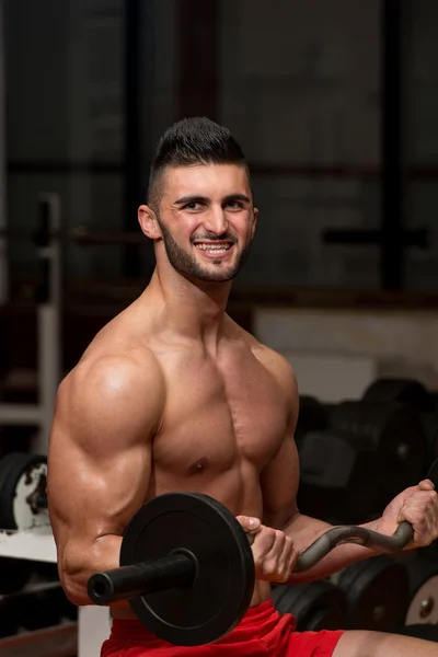 Hombre en el gimnasio ejercitando bíceps con barra — Foto de Stock
