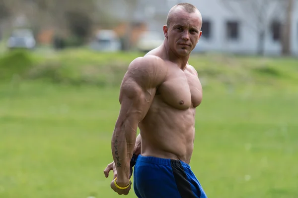 Bodybuilder effectuant des poses latérales de triceps dans le parc — Photo